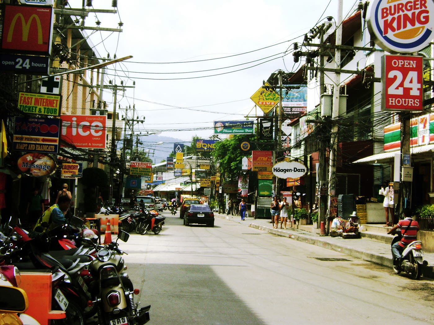 Chaweng Beach Road, the strip behind the sand. Photo: ThomasSD, Wikimedia Commons, public domain. Chaweng Beach Road, Koh Samui, a busy strip of shops and signs behind the beach