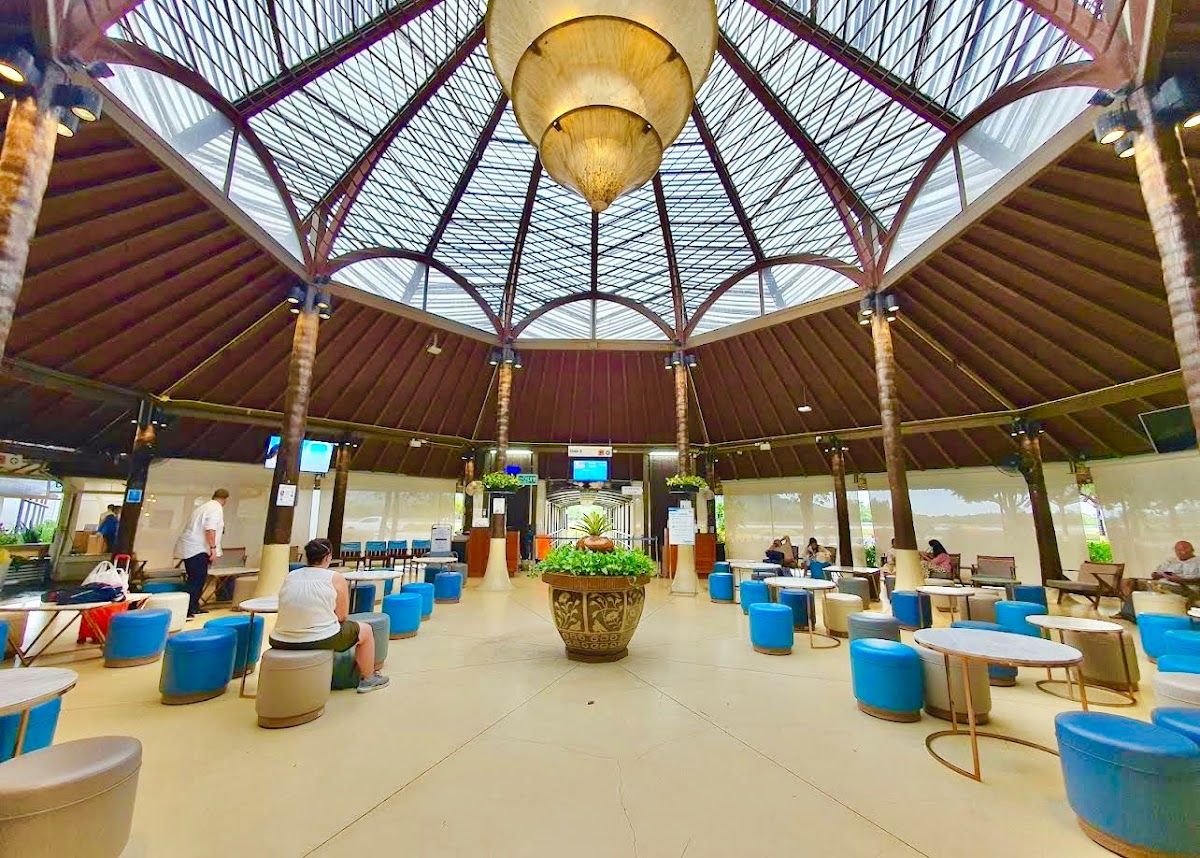Interior of Samui Airport's open-air terminal building, with its lattice glass roof, tropical plants, and blue seating