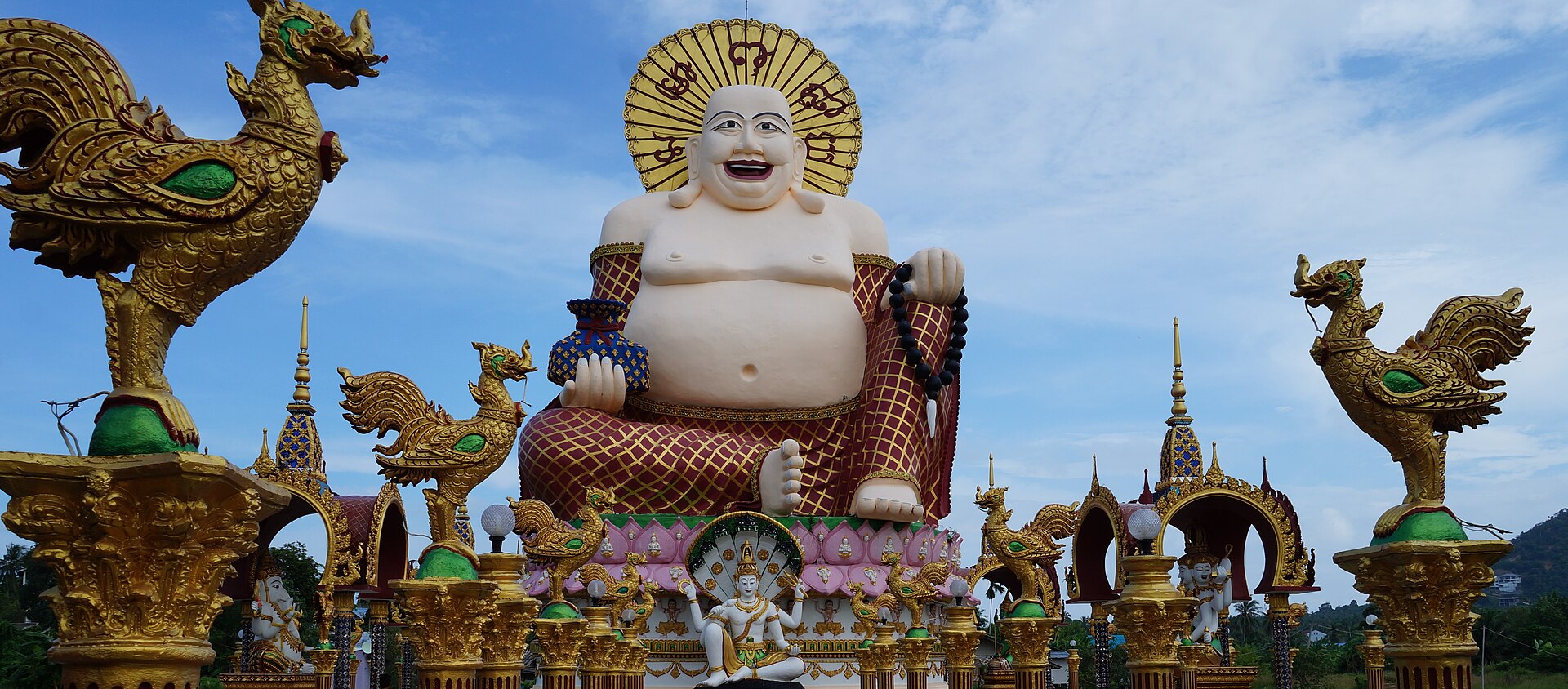 The 18-armed white Guanyin at Wat Plai Laem, Koh Samui, standing on a lotus in the lake with temple roofs behind
