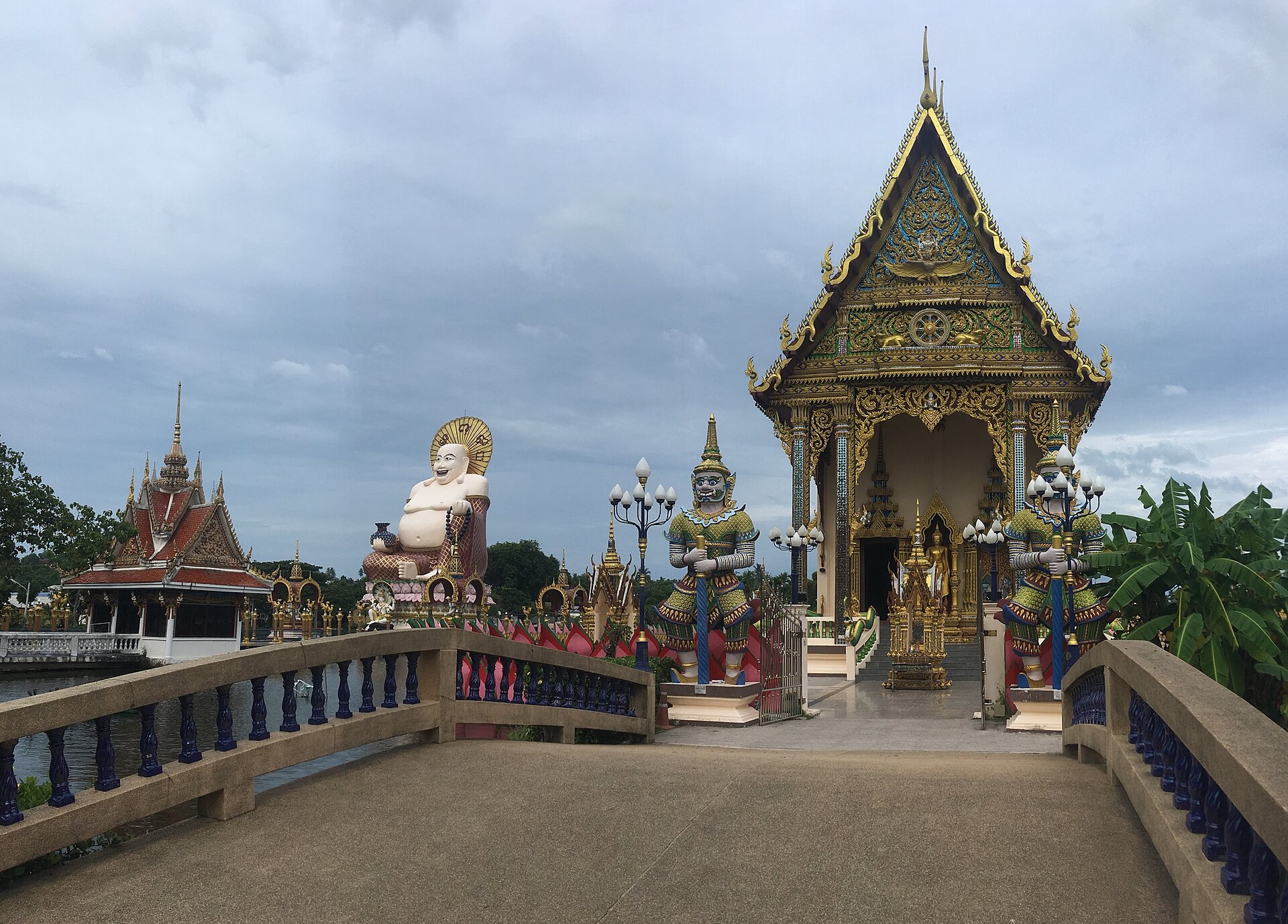 The large laughing Buddha at Wat Plai Laem, a seated smiling figure on a platform over the water